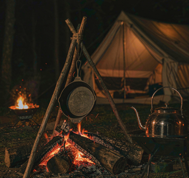 Campfire with cast iron skillet and copper kettle at night